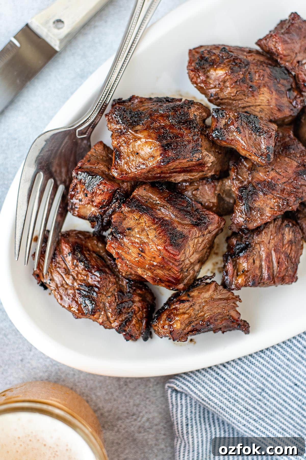 Beer Teriyaki Marinated Steak Tips for Grilling or Pan-Searing 2 Perfectly caramelized steak tips on a white serving plate pictured with a fork and knife.