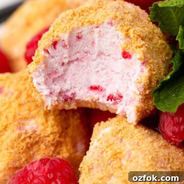 Raspberry cheesecake bites coated in graham cracker crumbs stacked on a plate.