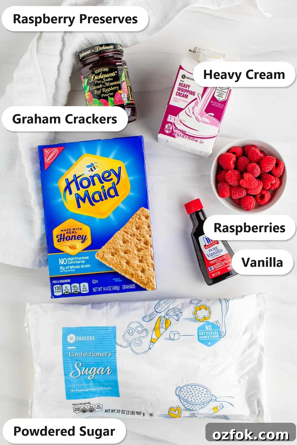 No-Bake Raspberry Icebox Cake Recipe for Summer Parties 3 Ingredients to make a Raspberry Icebox Cake laid out and labeled on a white cloth.