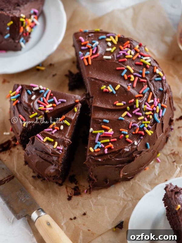 Angled image of sliced single layer chocolate cake on parchment paper with slices of cake on small dessert plates around it and a knife on parchment paper.
