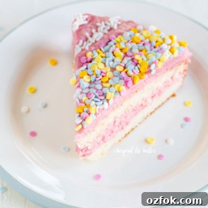 Slice of vanilla bean cake frosted with strawberry swiss meringue buttercream and topped with sprinkles on a dessert plate.