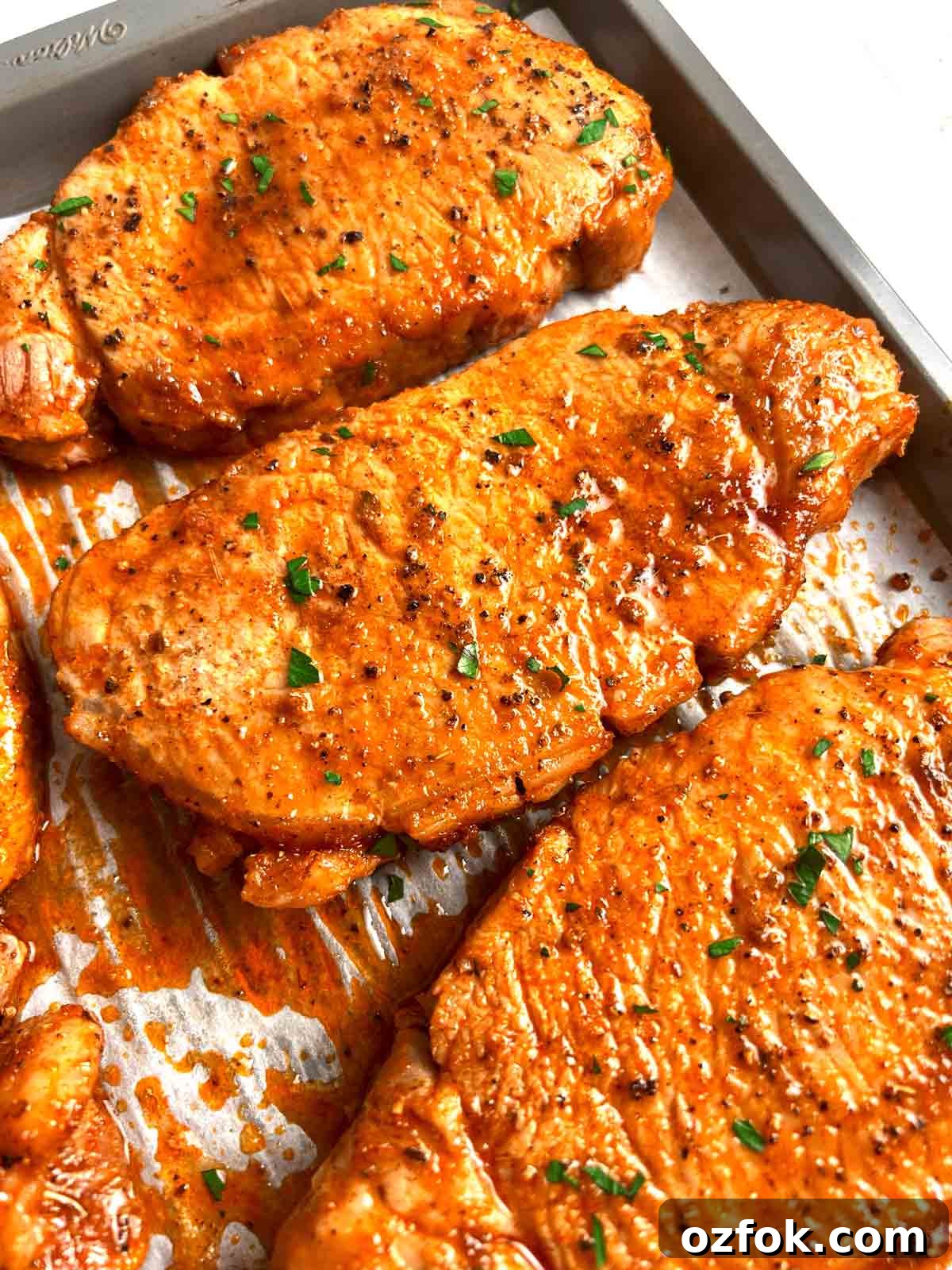 Juicy Oven-Baked Pork Chops with Garlic and Herbs 2 close up of baked pork chops with parsley sprinkled on top.
