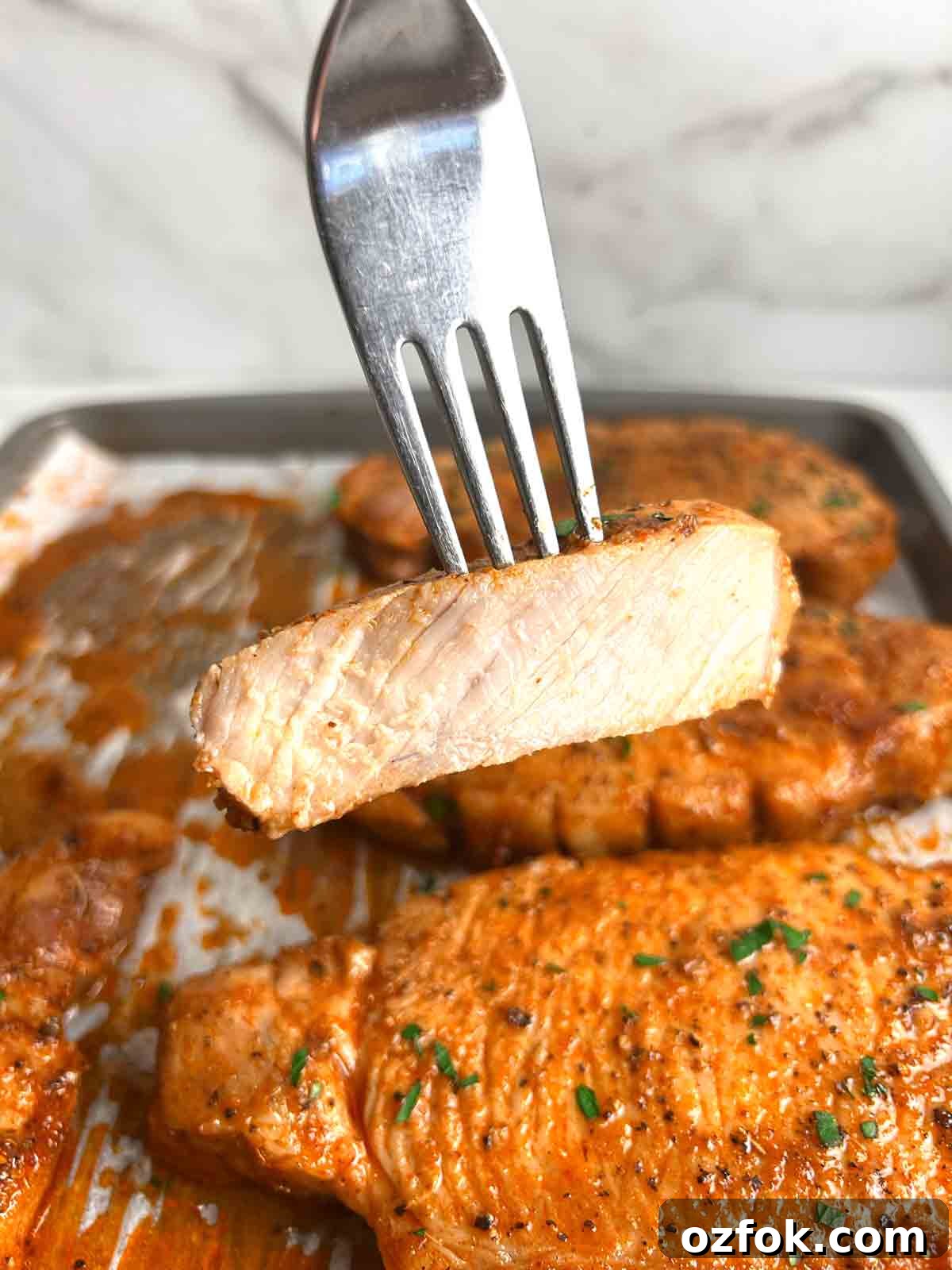 Juicy Oven-Baked Pork Chops with Garlic and Herbs 3 fork lifting slice of pork.