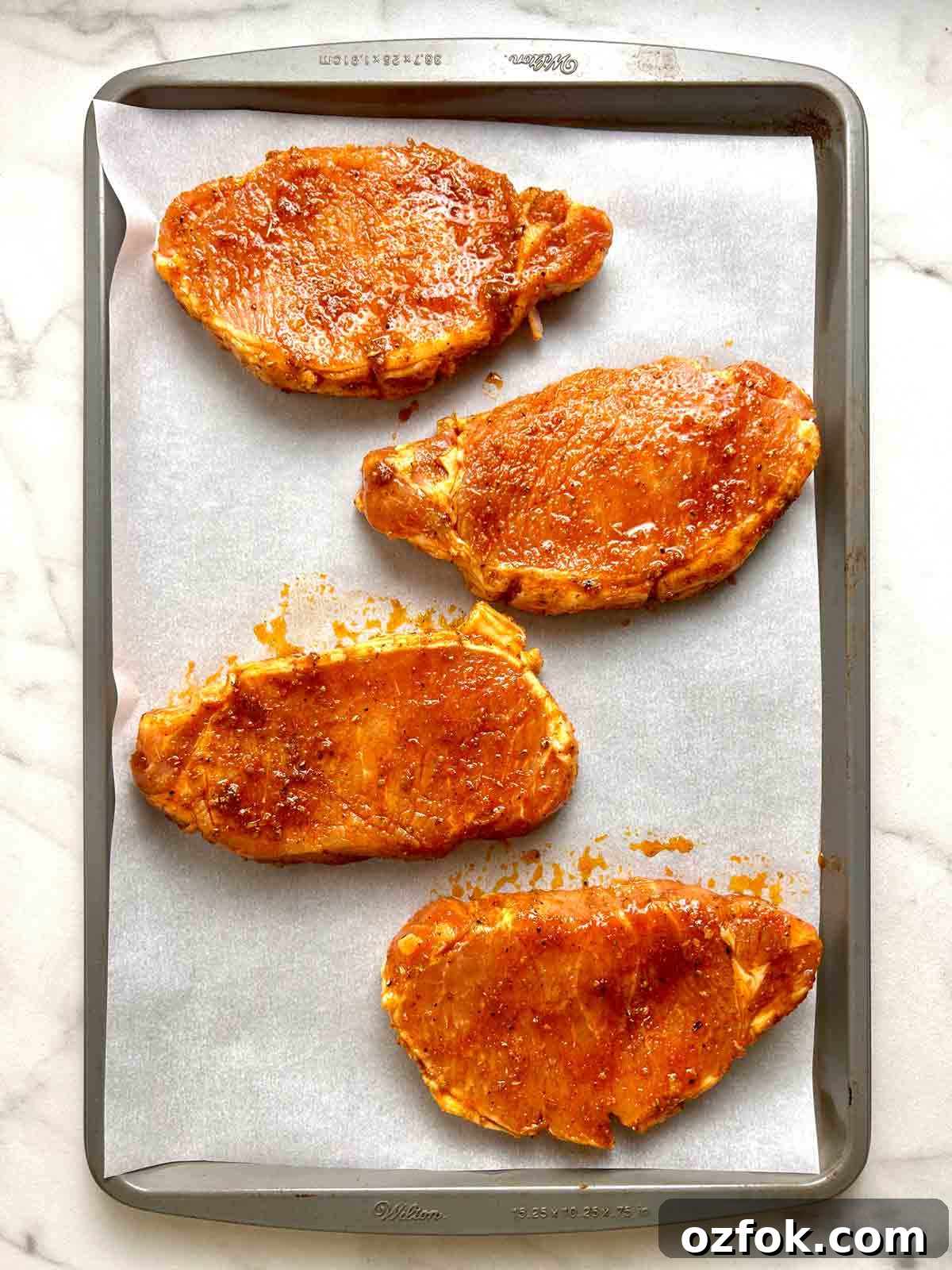 Juicy Oven-Baked Pork Chops with Garlic and Herbs 7 marinated pork chops arranged on baking sheet.