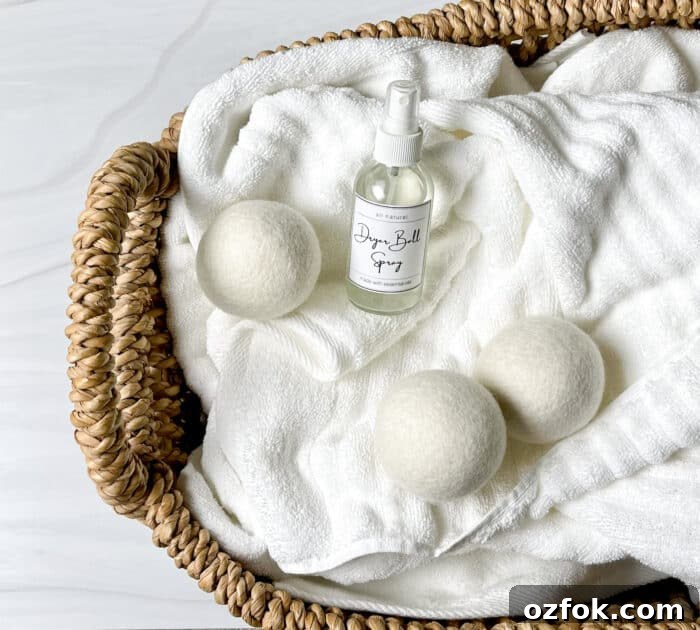 DIY Dryer Ball Spray with Essential Oils for Fresh Laundry 3 laundry basket filled with fluffy white towels -- on top of towels are 3 wool dryer balls and glass spray bottle of homemade dryer ball spray