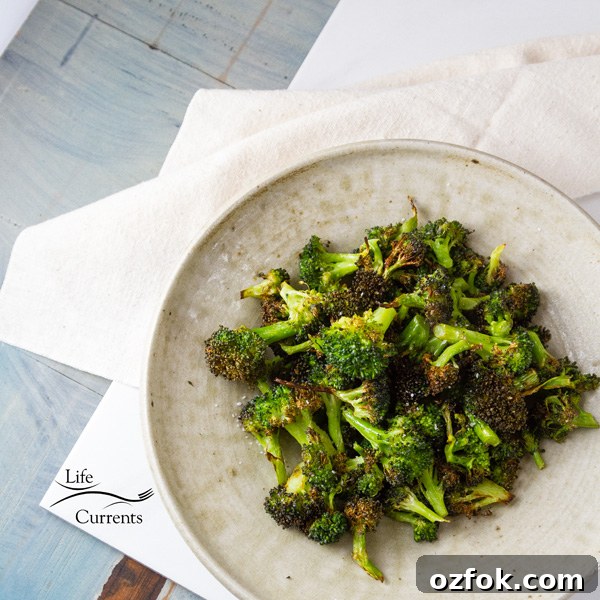 Crispy Air Fryer Roasted Broccoli Recipe 4 square crop top down of Air Fryer Roasted Broccoli in a white bowl on a white cloth with a blue counter top