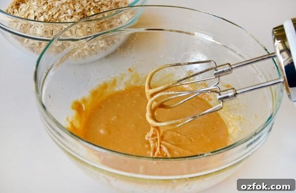 Homemade Peanut Butter Granola Bars Recipe – Chewy No-Bake Snack 4 Large glass bowl with peanut butter, honey, egg, oil and vanilla extract with a handheld beater