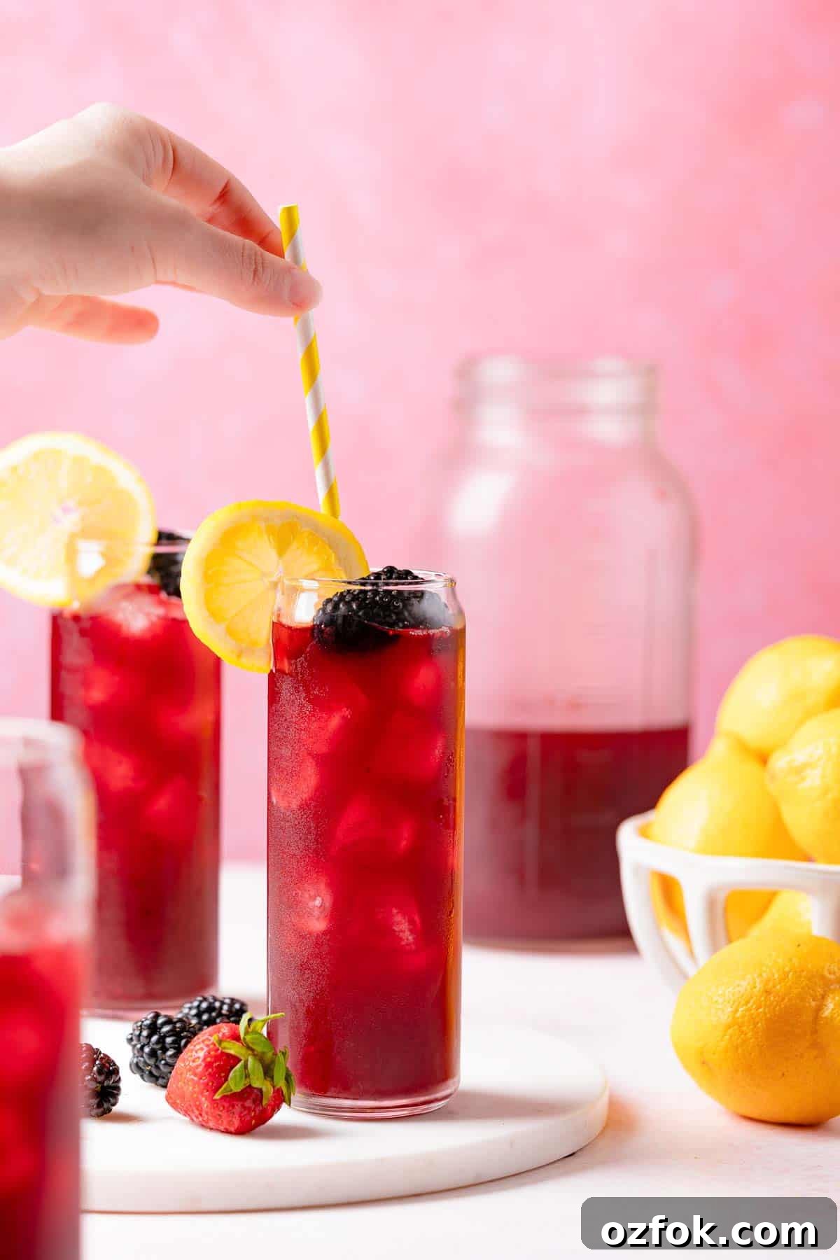 Refreshing Berry Lemonade Recipe: Bright Summer Drink Guide 2 straw being placed in glass of berry lemonade next to two other glasses of lemonade.