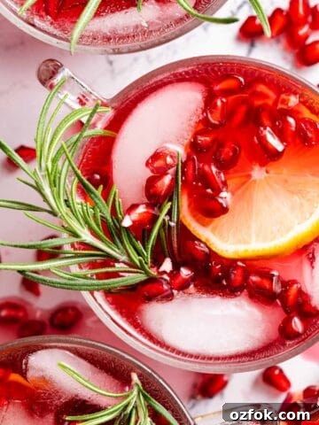 pomegranate cranberry punch in glass garnished with pomegranate seeds and rosemary