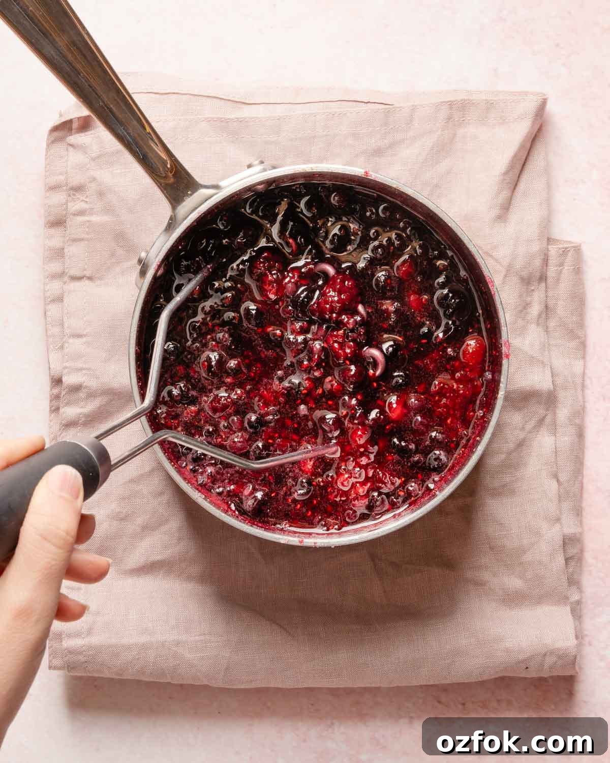 Refreshing Berry Lemonade Recipe: Bright Summer Drink Guide 6 potato masher mashing cooked berries in a small pot.