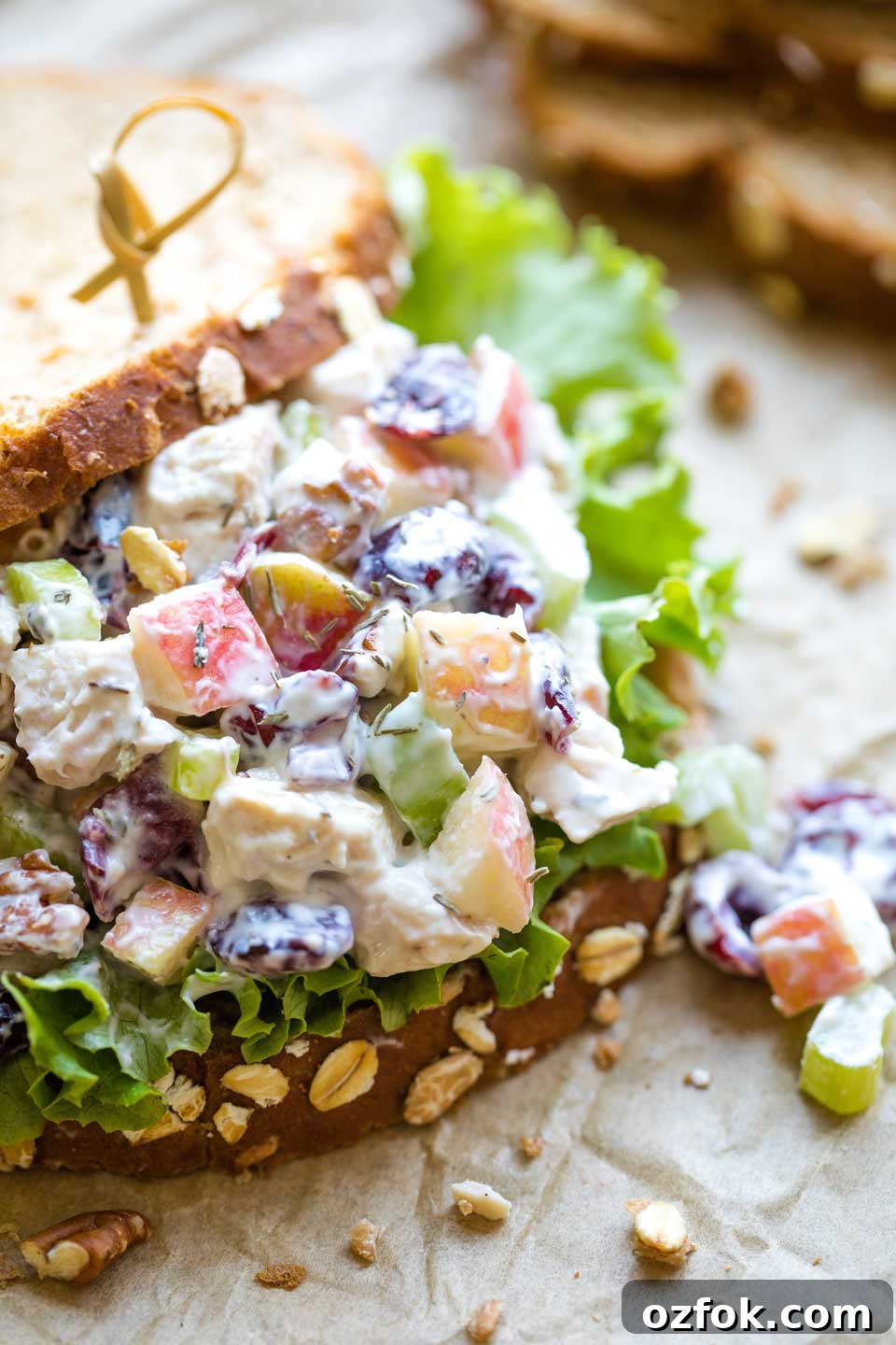 Closeup of a sandwich on parchment, with the top slice of bread sliding back so you can see the turkey salad piled inside.