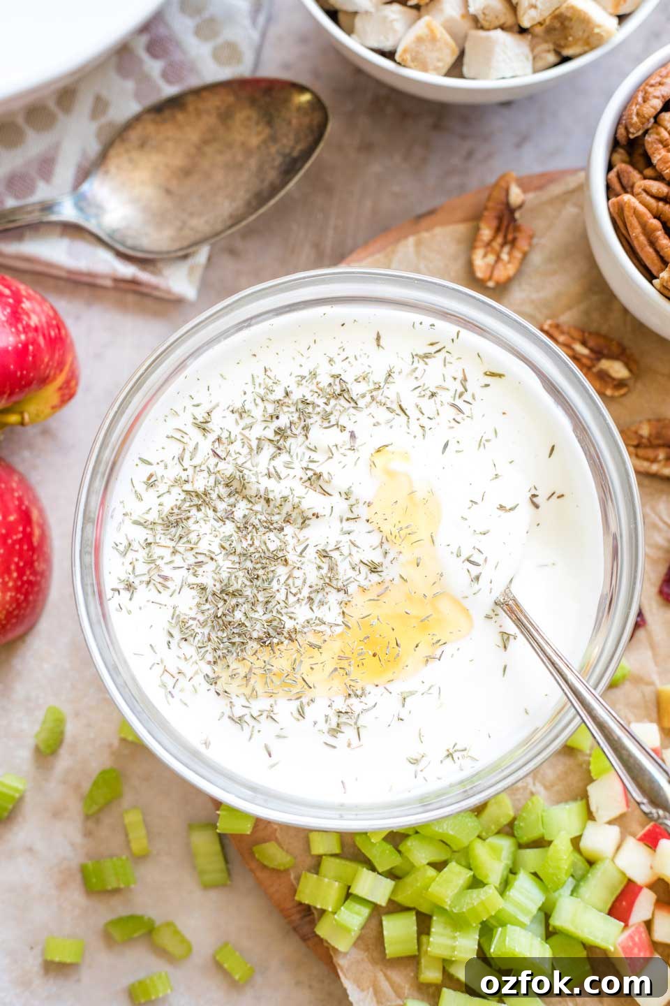 Overhead photo of the dressing ingredients in a glass bowl, unmixed but with a spoon in it, with other turkey salad ingredients scattered nearby.