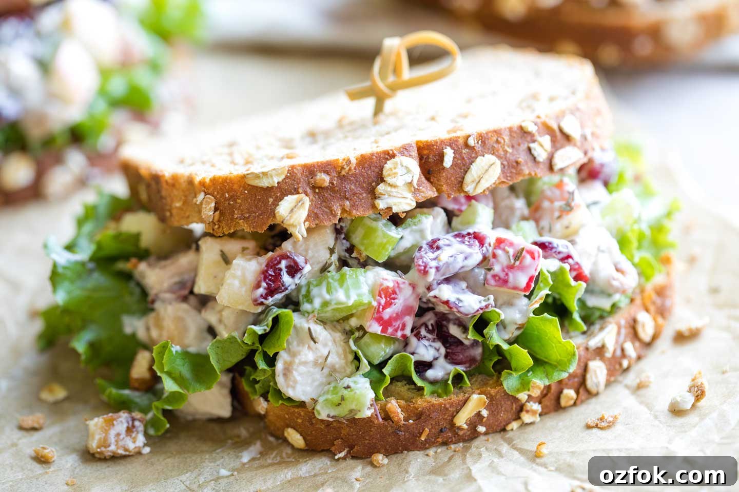 One finished sandwich, made with grainy bread and leaf lettuce, held together by a curly bamboo toothpick and sitting on parchment.