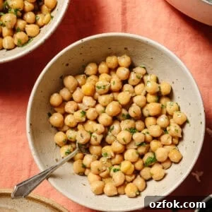 overhead view of cooked chickpeas with parsley in a bowl with a silver spoon in it.