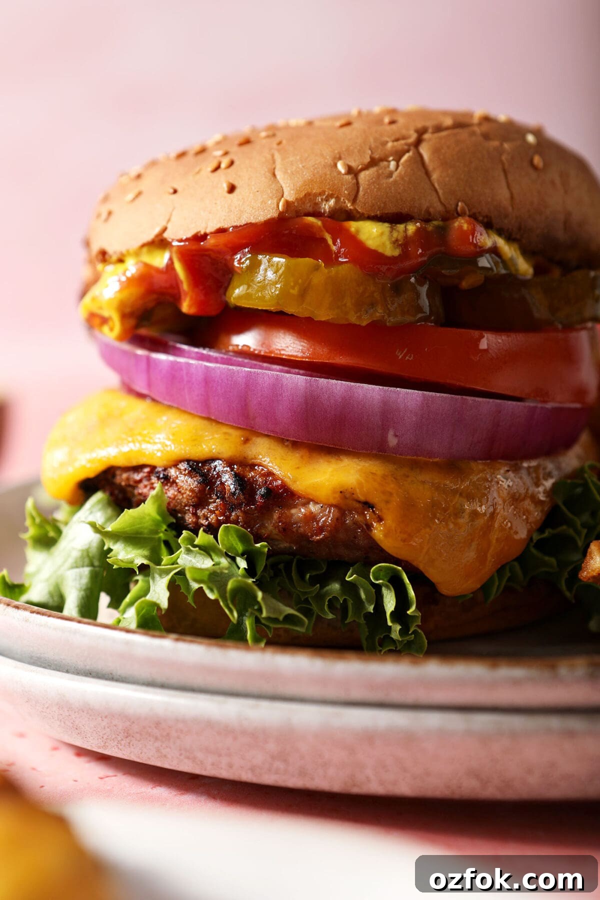 20+ Fourth of July Grilling Recipes for Your Backyard BBQ 12 Close up of a grilled turkey burger stacked with toppings on a grey plate on a pink surface