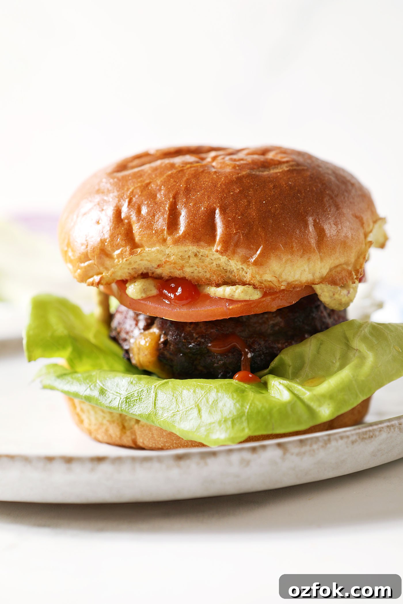 20+ Fourth of July Grilling Recipes for Your Backyard BBQ 3 A juicy Lucy burger on a grey plate all dressed up before biting into it