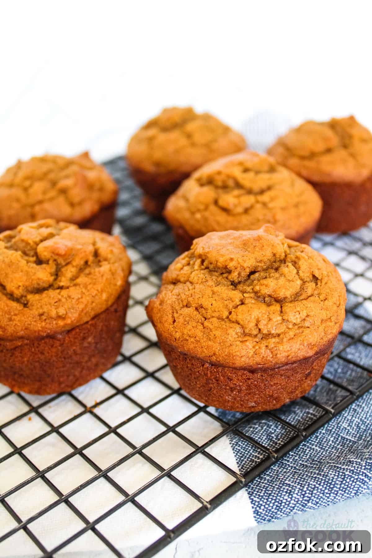 Six sweet potato muffins on a wire rack on top of a kitchen towel.