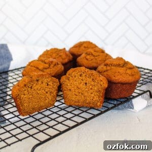 Six sweet potato muffins on a wire rack, the front one cut open in half, a blue striped kitchen towel under them.