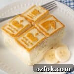 Slice of banana pudding on a white plate with sliced bananas and a fork.