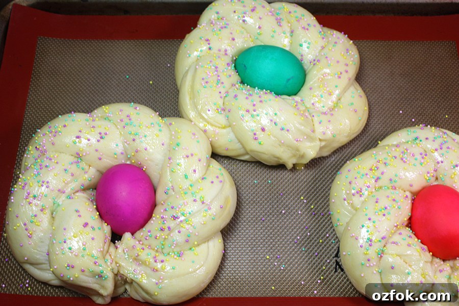 Risen, shaped dough with dyed eggs in the middle on a baking sheet.