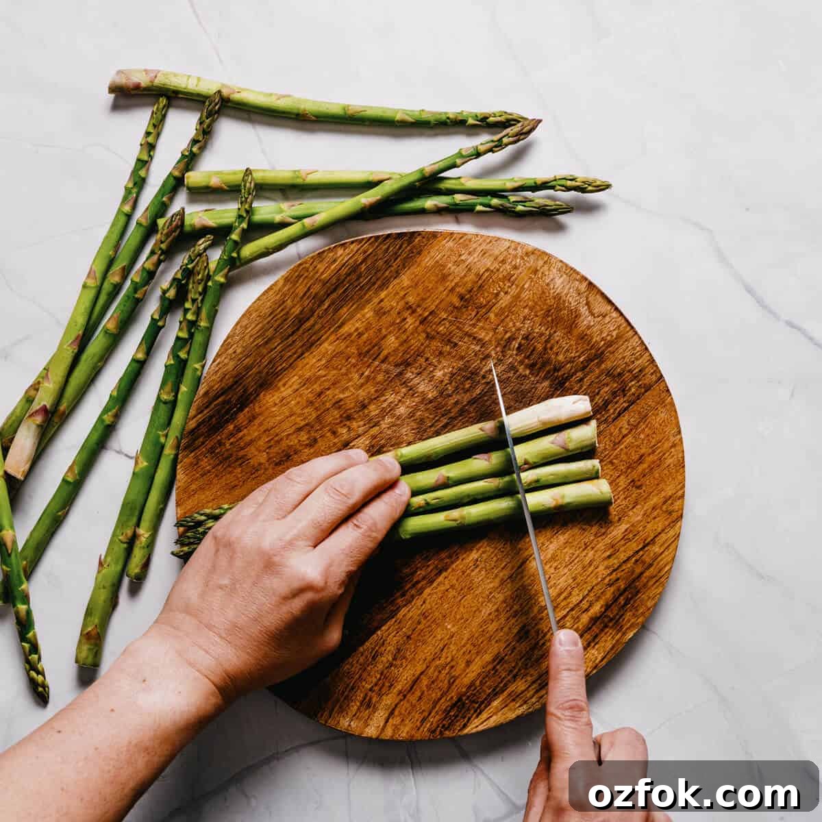 Foil-Grilled Asparagus with Lemon and Garlic 5 asparagus spears being cut with a knife on a round wooden chopping board.