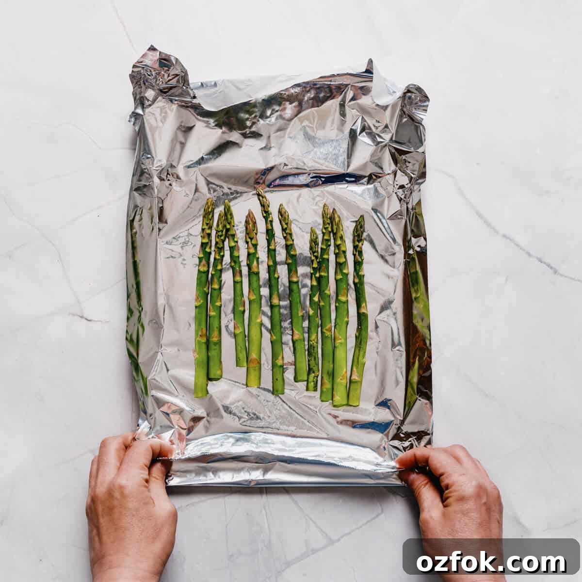Foil-Grilled Asparagus with Lemon and Garlic 6 a pair of hands sealing an aluminum foil packet filled with asparagus.