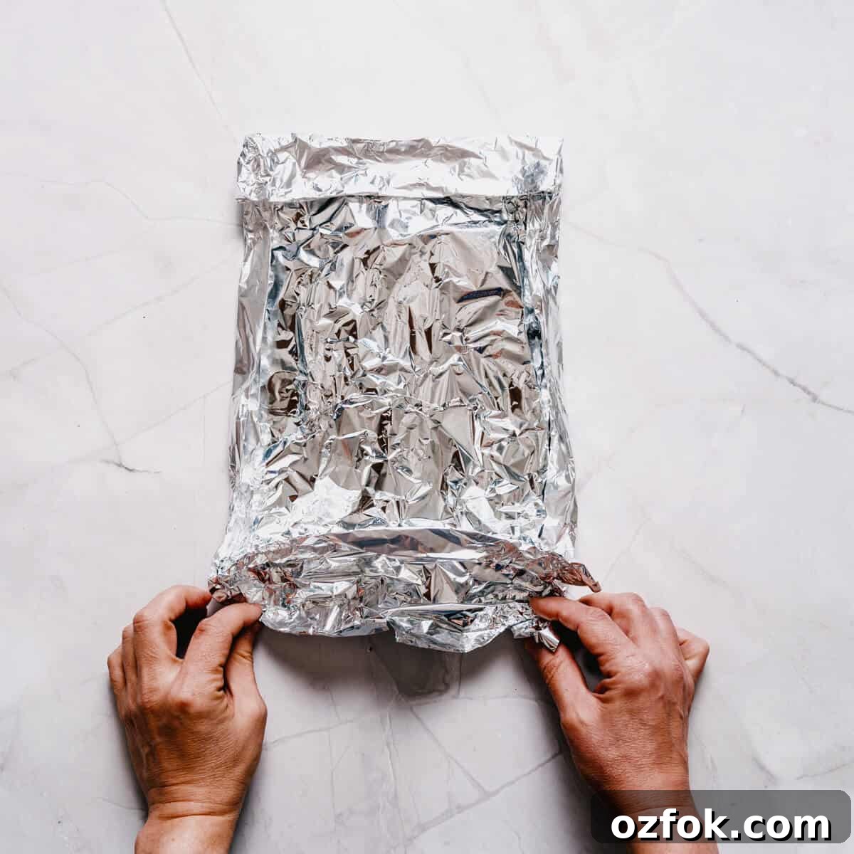 Foil-Grilled Asparagus with Lemon and Garlic 8 a pair of hands sealing an aluminum foil pack.