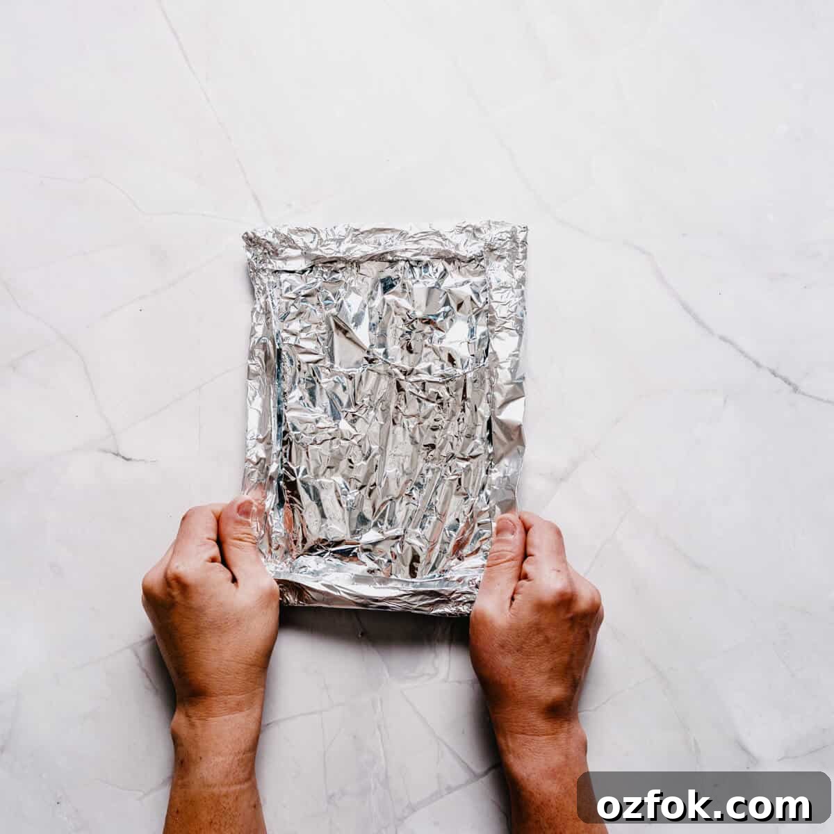 Foil-Grilled Asparagus with Lemon and Garlic 9 a pair of hands holding a sealed aluminum foil packet.