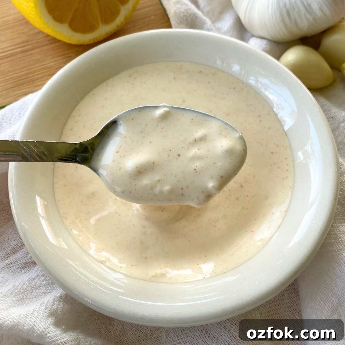 Lemon Garlic Aioli: Homemade Creamy Sauce Recipe 5 Spoon lifting homemade lemon garlic aioli out of a small bowl.