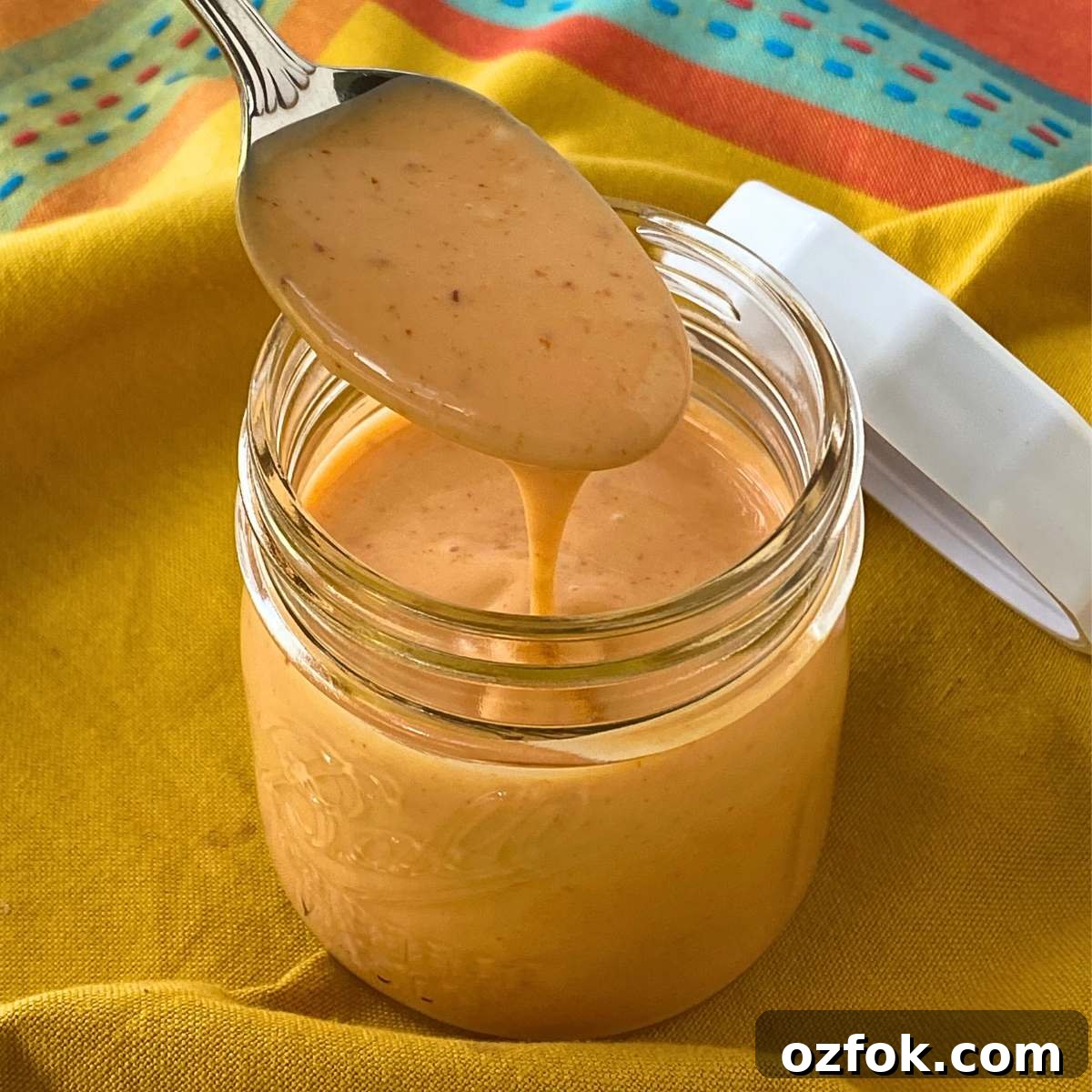 Spoon lifting homemade bang bang sauce from a small mason jar.
