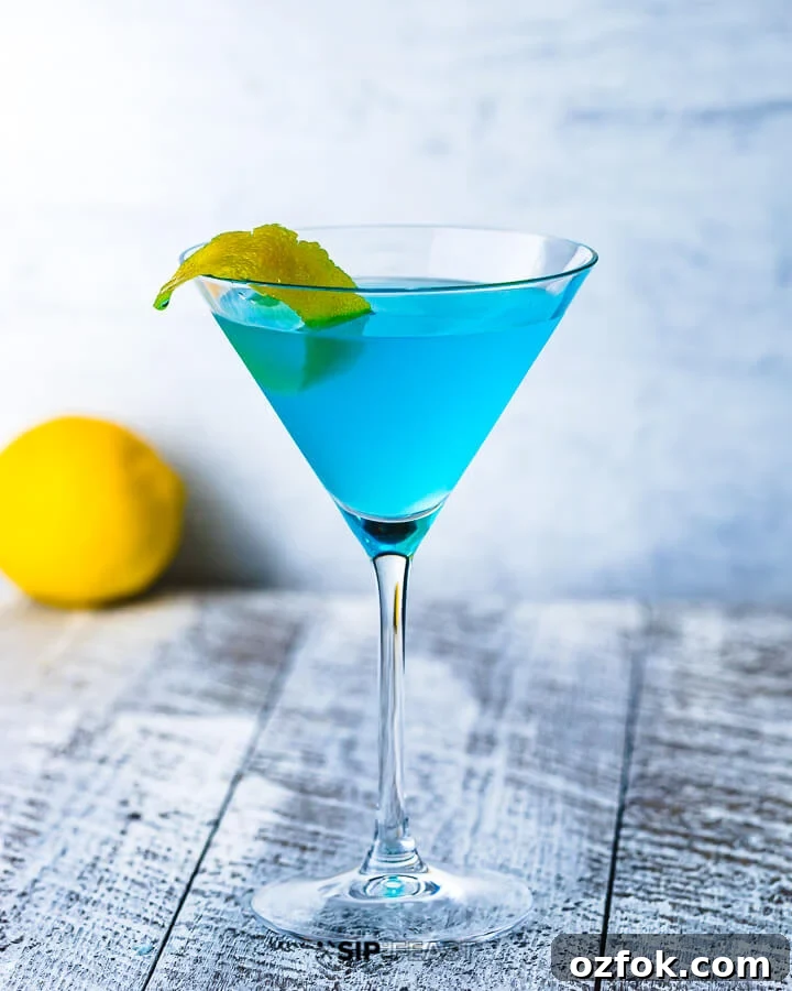 A martini glass with the Angelo Azzuro cocktail and a lemon in the background.