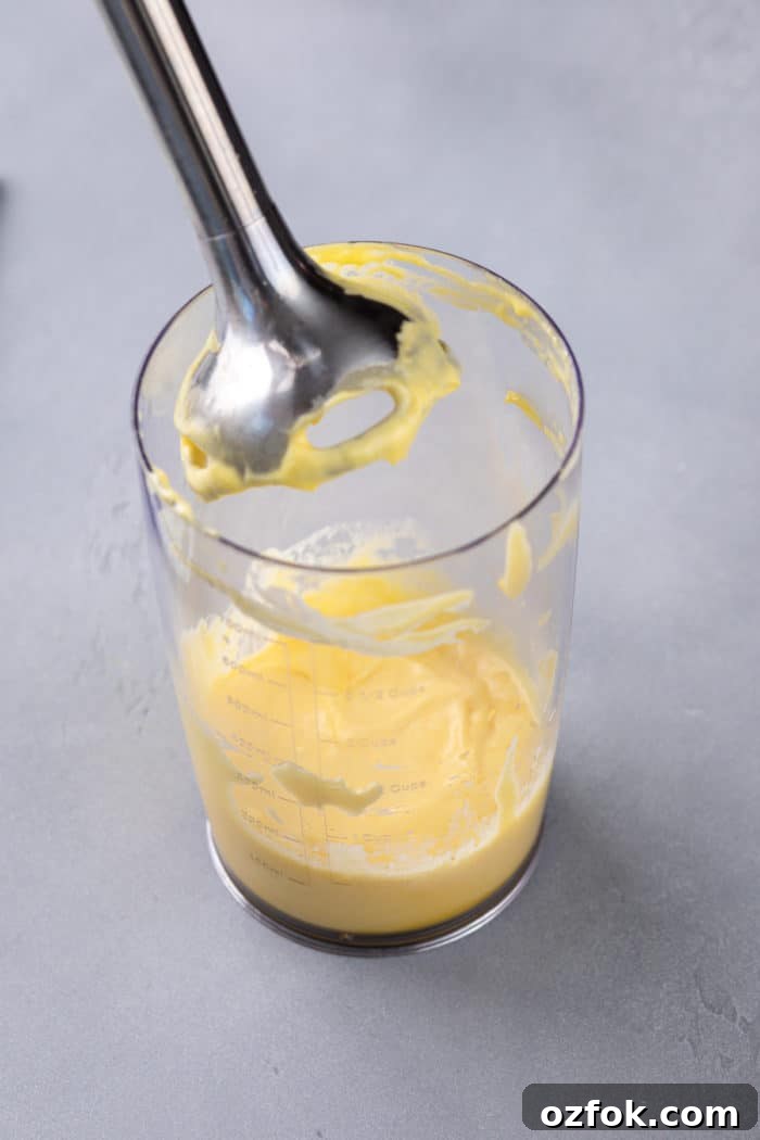 Classic Eggs Benedict Recipe: How to Make Perfect Hollandaise and Poached Eggs 5 Freshly made hollandaise sauce in a cup with an immersion blender.