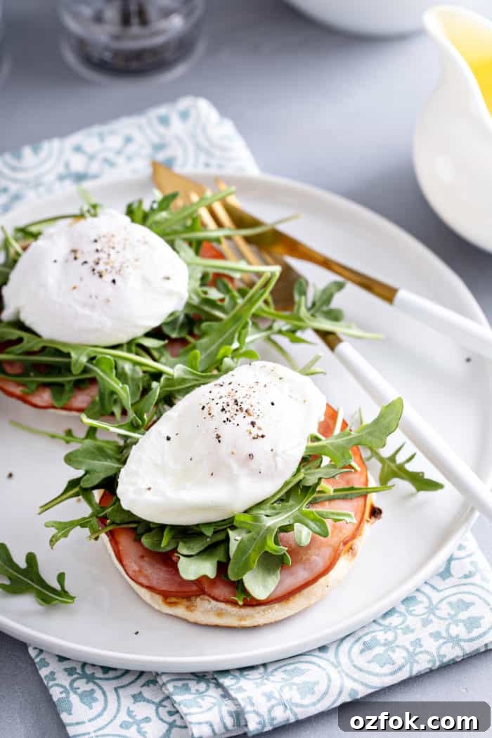 Classic Eggs Benedict Recipe: How to Make Perfect Hollandaise and Poached Eggs 8 Poached eggs on top of english muffin, canadian bacon, and arugula, waiting to be topped with hollandaise.