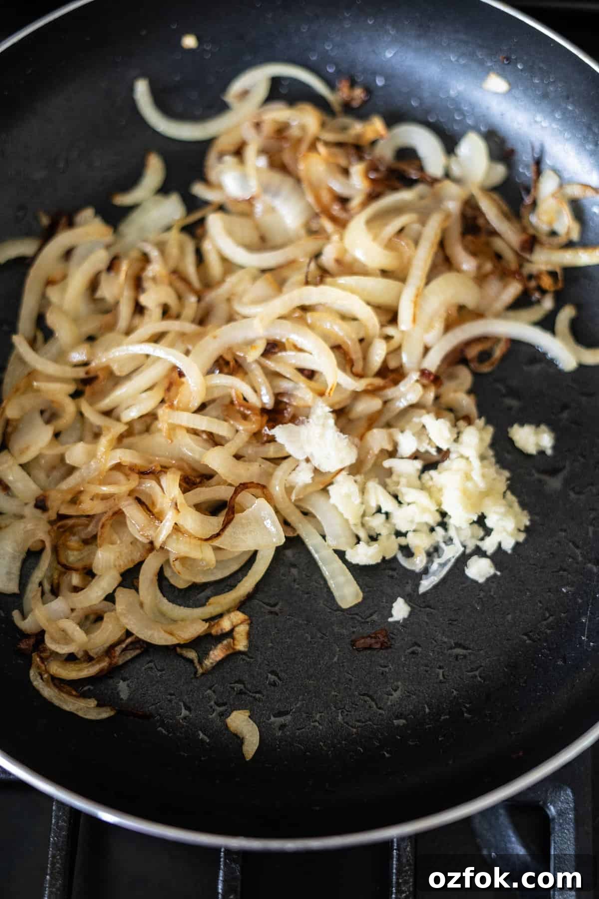 Keto French Onion Dip Recipe for Low-Carb Snacking 4 Sliced onions and minced garlic cooking in a black frying pan on a stove.