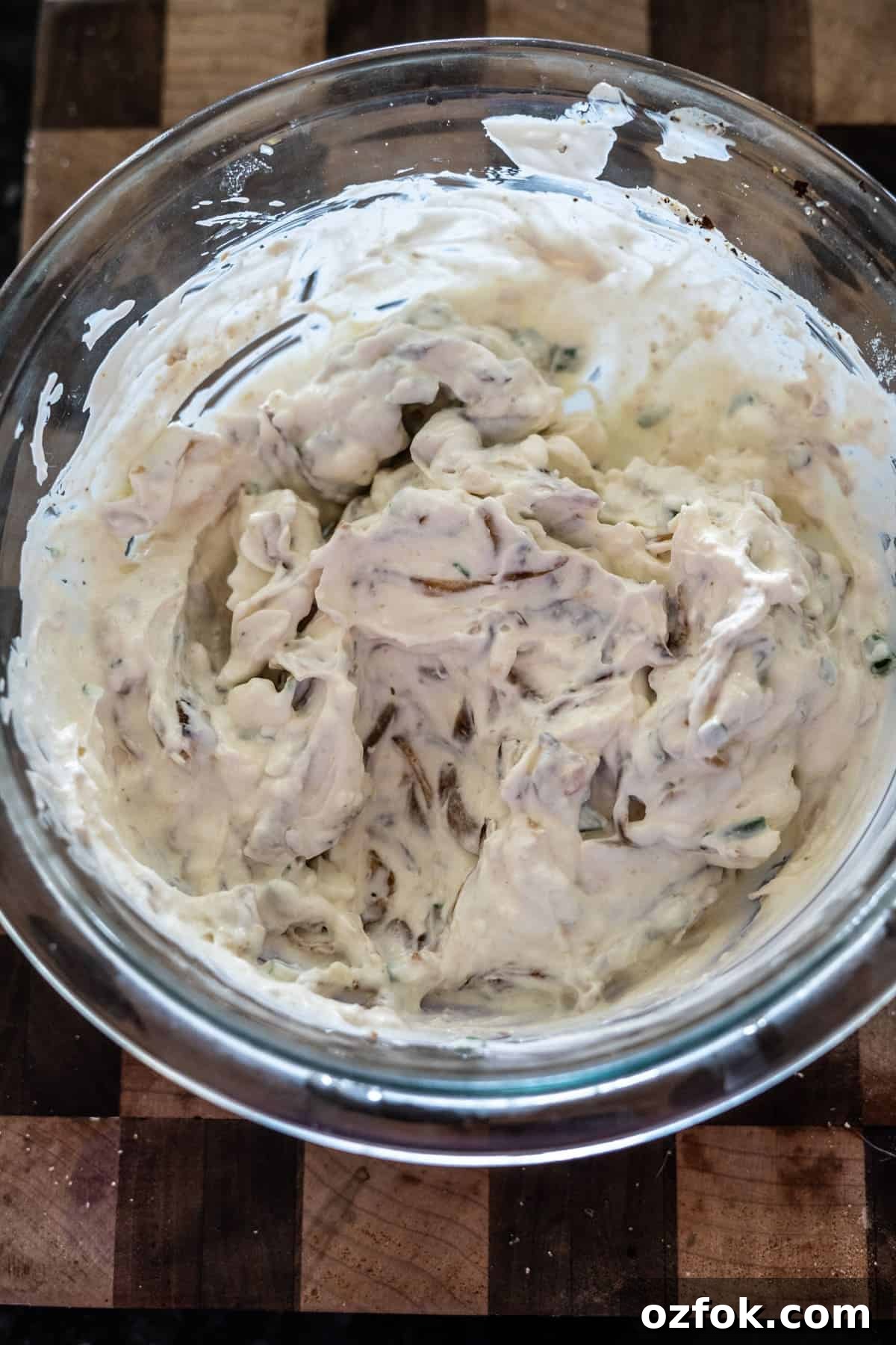 Keto French Onion Dip Recipe for Low-Carb Snacking 7 A glass bowl filled with a creamy, textured mixture sits on a wooden surface.