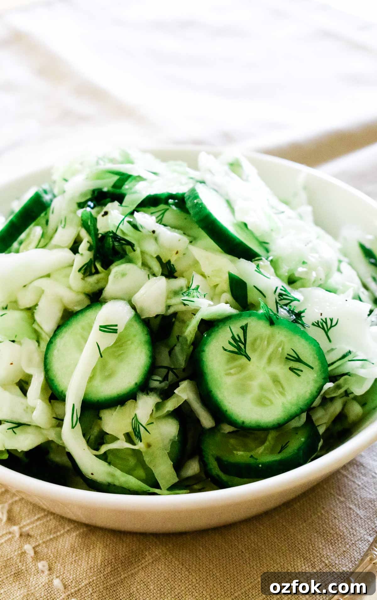 Shredded cabbage with cucumbers in a white bowl.