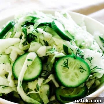 Shredded cabbage with cucumbers in a white bowl.