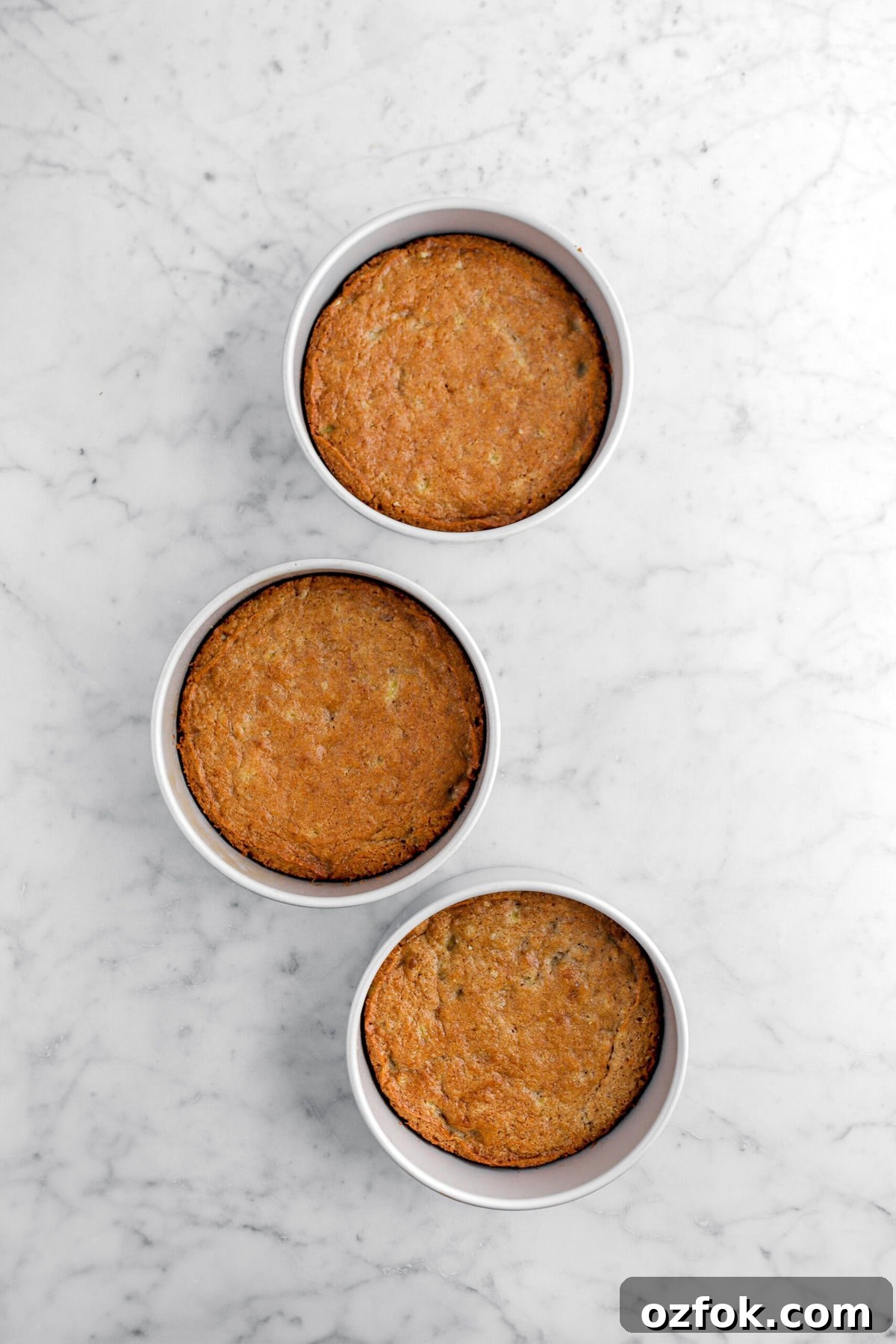 three baked cake layers in cake pans.