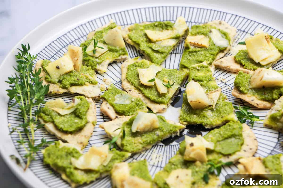 Olive & Artichoke Canapés: Elegant Party Appetizer Recipe 2 photo of a black and white plate with Artichoke and Tapenade Canapes on it and sprinkled with thyme leaves and a sprig of thyme on the side, on a white and grey marble top.