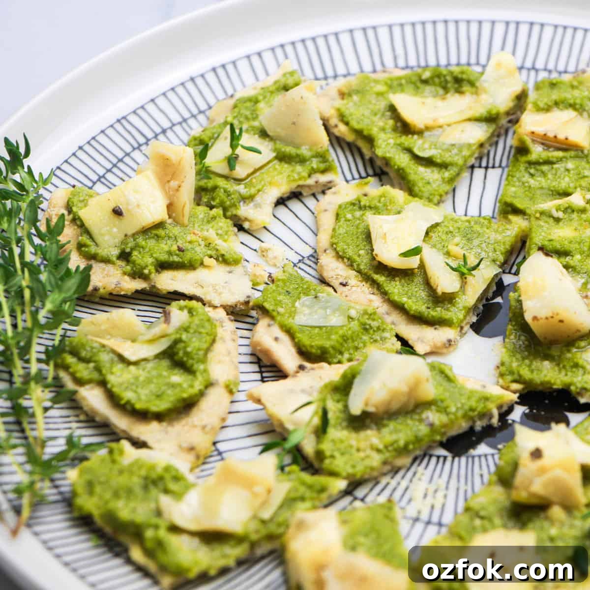 Olive & Artichoke Canapés: Elegant Party Appetizer Recipe 4 photo of a black and white plate with Artichoke and Tapenade Canapes on it and sprinkled with thyme leaves and a sprig of thyme on the side, on a white and grey marble top.
