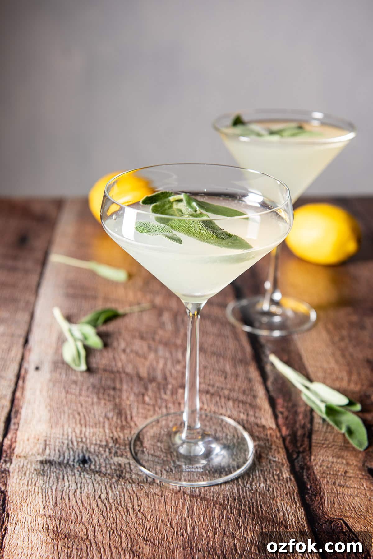 Sage Limoncello Martini Recipe — Citrus Cocktail with Herbal Twist 2 wooden boards with the martini glasses filled with the cocktail along with lemons and sage leaves