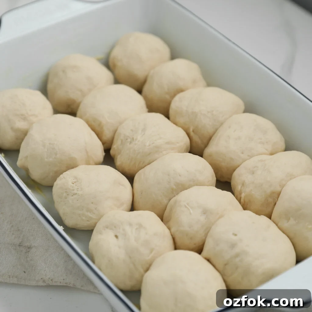 A white rectangular baking dish filled with sixteen evenly arranged, uncooked dough balls.