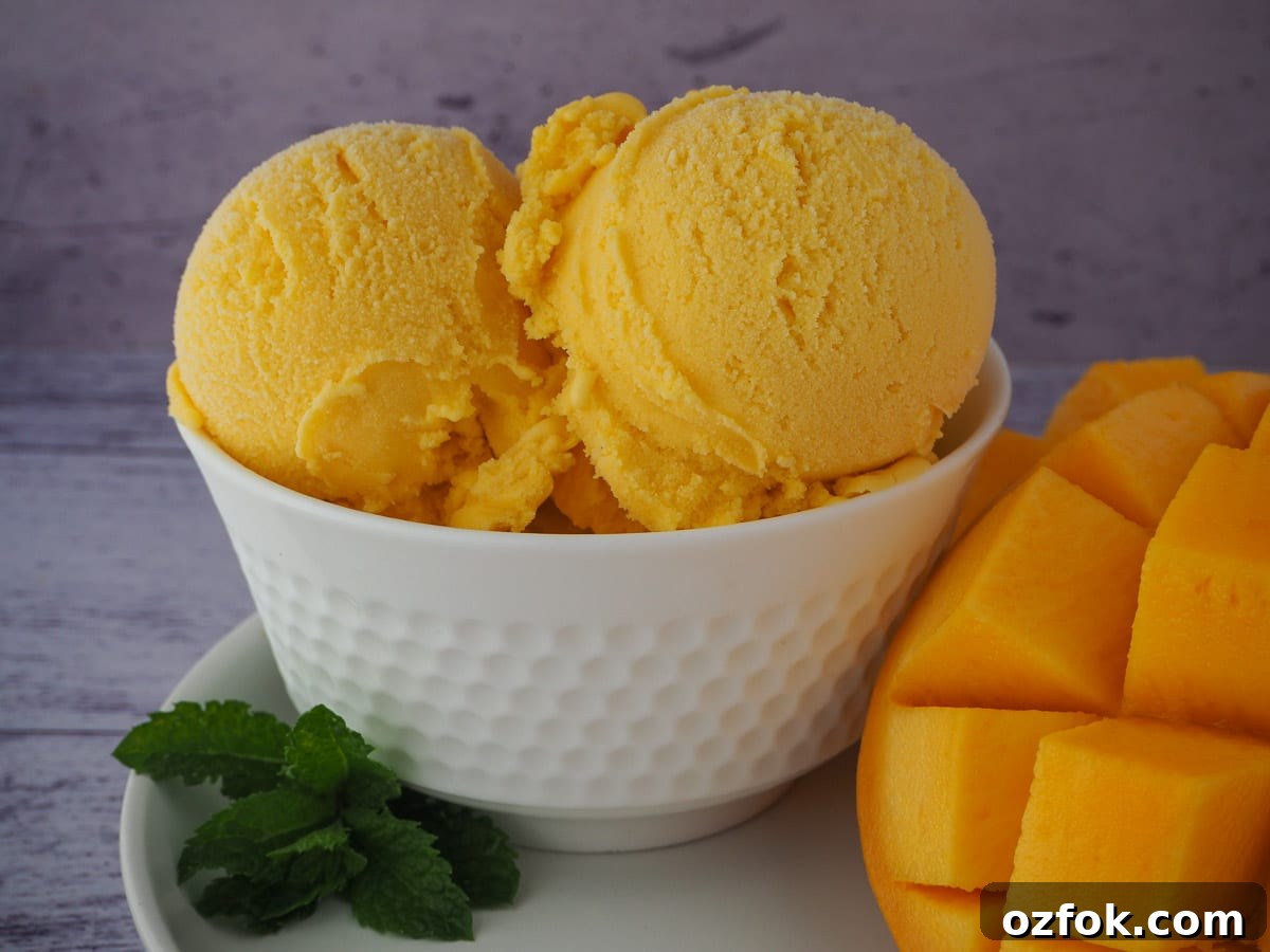 Creamy Mango Ice Cream Recipe: Fresh Mango Frozen Dessert 15 Scoops of mango ice cream in a white bowl with fresh mint and mango.