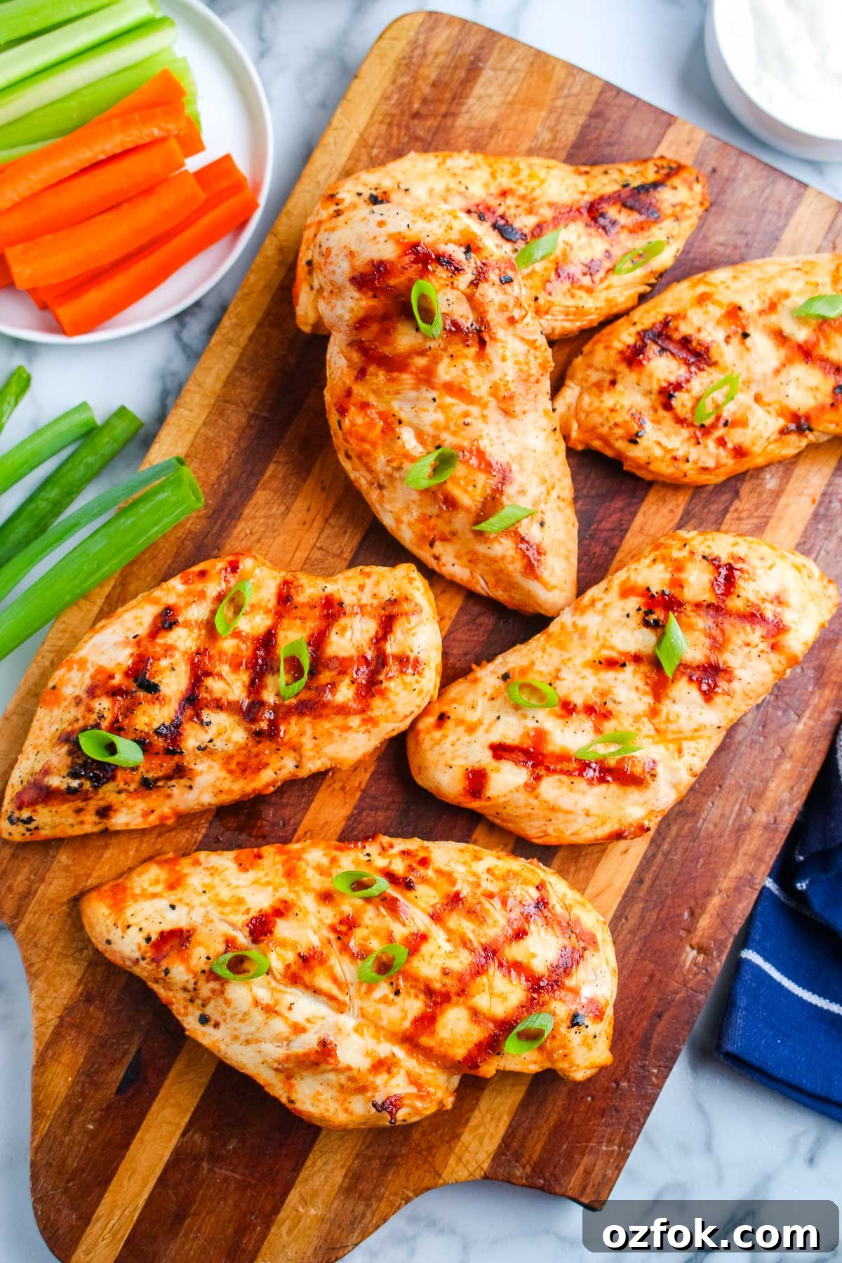 Grilled Buffalo Chicken Breasts with Tangy Blue Cheese Dip 2 Grilled buffalo chicken breasts arranged on a wooden cutting board with green onions, carrots, celery, and ranch dressing.
