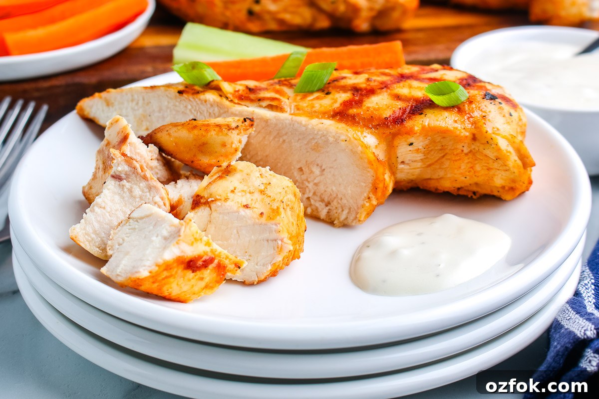 Grilled Buffalo Chicken Breasts with Tangy Blue Cheese Dip 3 Sliced grilled buffalo chicken breast served with ranch dressing and green onions on a white plate.