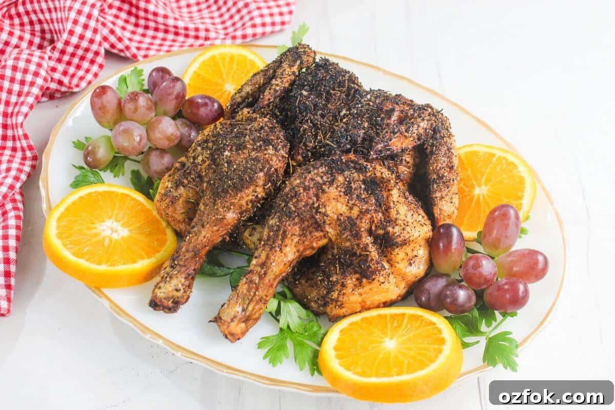 Crispy Air Fryer Spatchcock Chicken Recipe for Juicy Results 2 A roasted, seasoned chicken is served on a white platter with orange slices, red grapes, fresh parsley, and a red gingham cloth in the background.