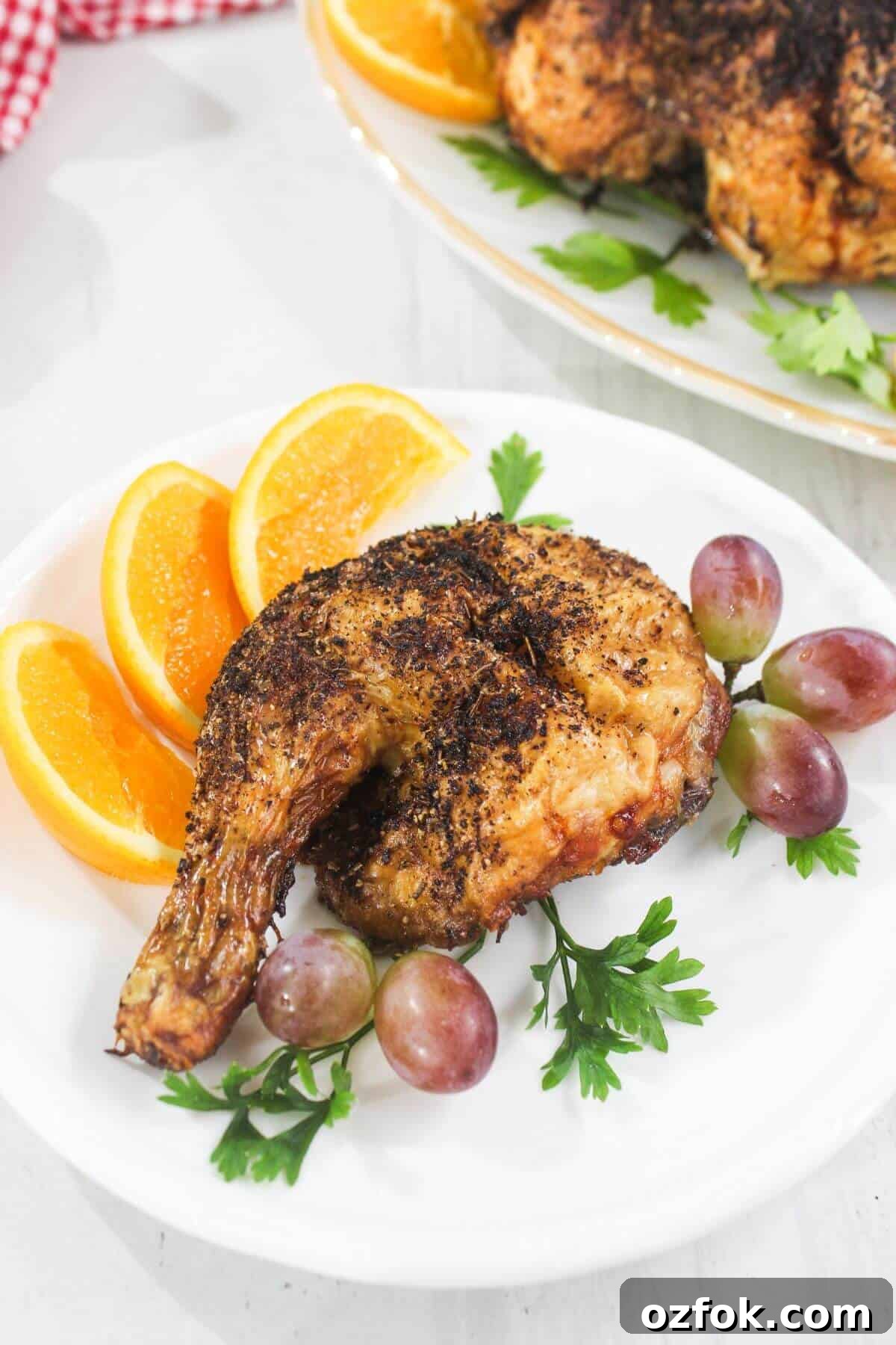 Crispy Air Fryer Spatchcock Chicken Recipe for Juicy Results 11 A cooked chicken leg quarter is served on a white plate with orange slices, red grapes, and fresh parsley as garnish.