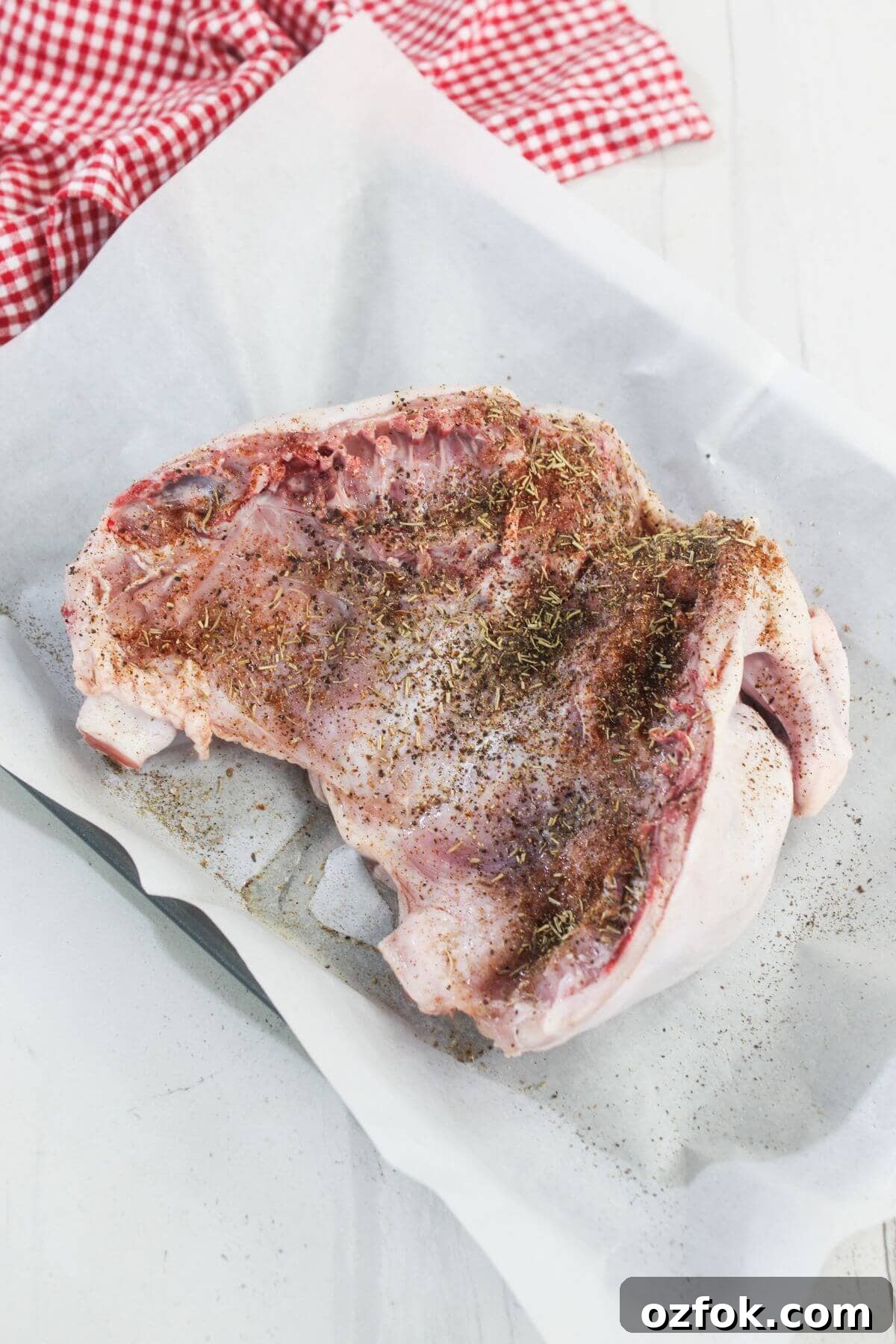 Crispy Air Fryer Spatchcock Chicken Recipe for Juicy Results 5 Raw turkey breast with skin, sprinkled with herbs and spices, placed on parchment paper in a baking dish; red checked cloth in background.
