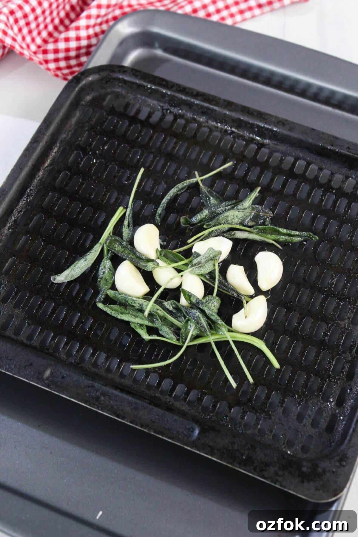 Crispy Air Fryer Spatchcock Chicken Recipe for Juicy Results 6 Whole garlic cloves and fresh sage leaves arranged on a black grill pan, ready to be roasted; a red and white checkered cloth is in the background.