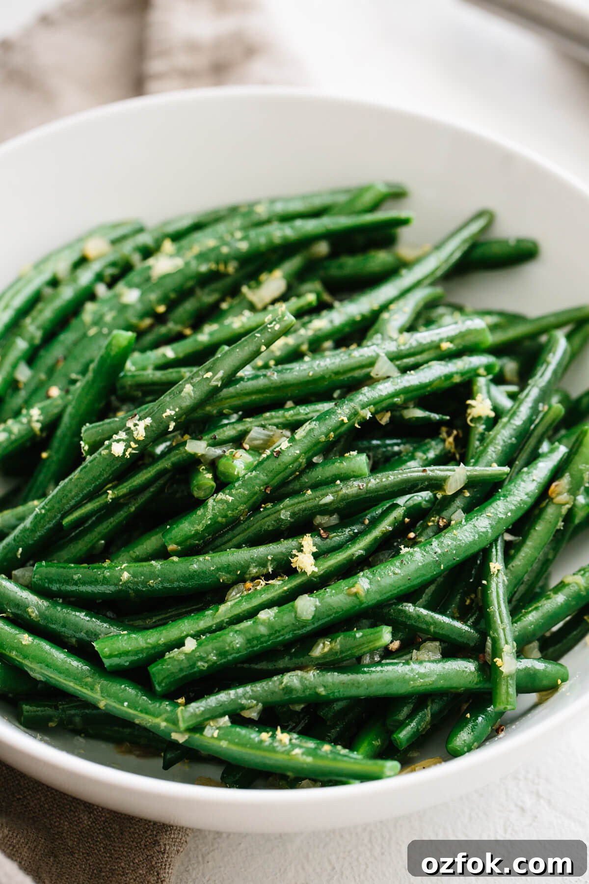 Green beans garnished with shallots and lemon in a white bowl.